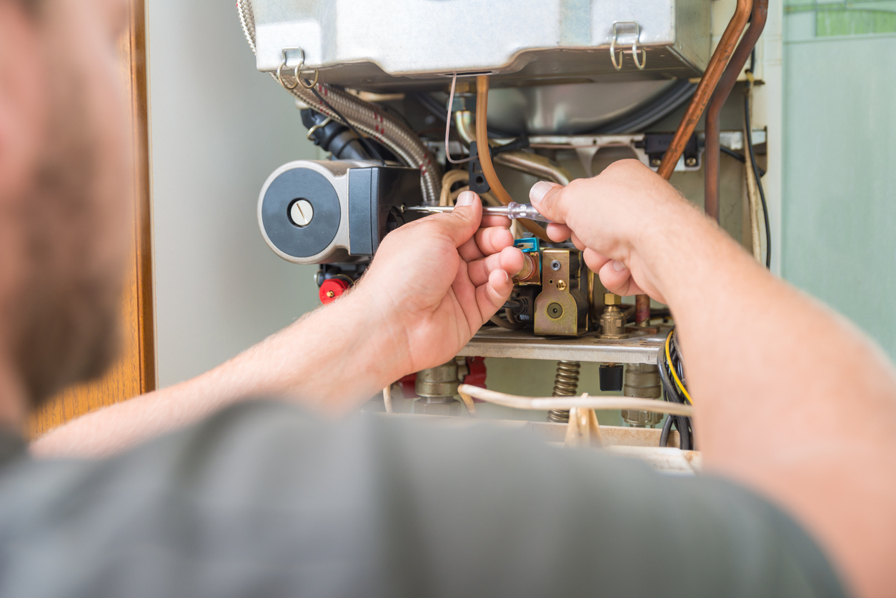 Technician using a screwdriver, performing maintenance on a gas furnace.